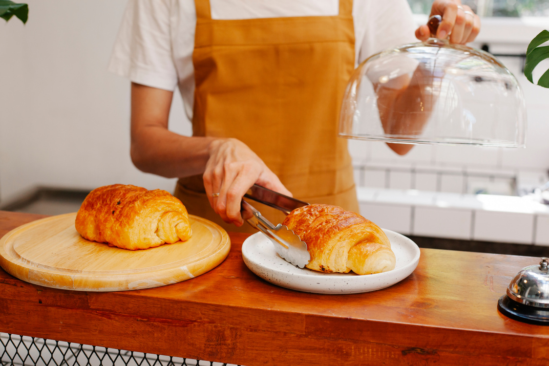 Crop baker putting appetizing puff on plate in cafeteria